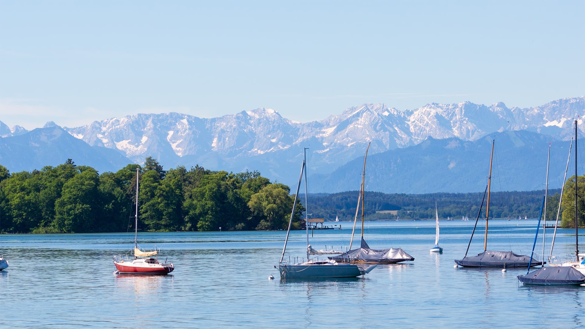 Idyllischer Starnberger See mit Segelbooten vor Alpenpanorama, Arbeitsumgebung am Bürostandort Keller Immobilien Berg.
